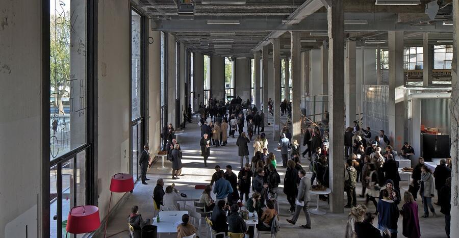 A view of the ground floor hall of the Palais de Tokyo, full of visitors engaging with an exhibition.