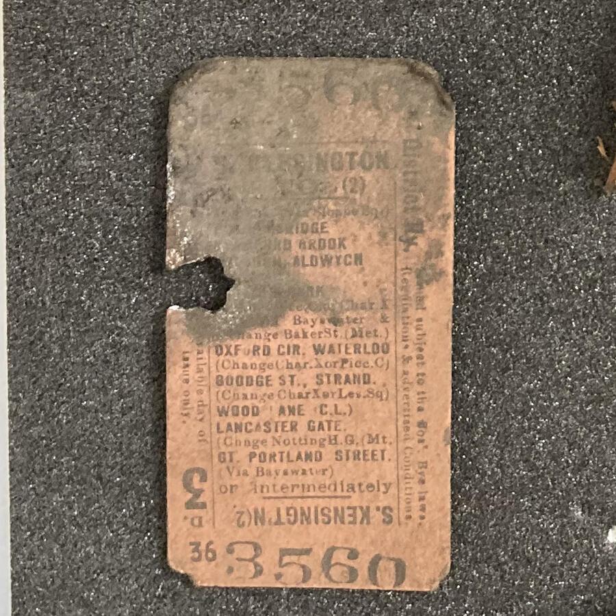A close up of the discovering tube ticket, made of orange card and tarnished to the top. A punch hole, left by a ticket conductor, can be seen on the left of the card.